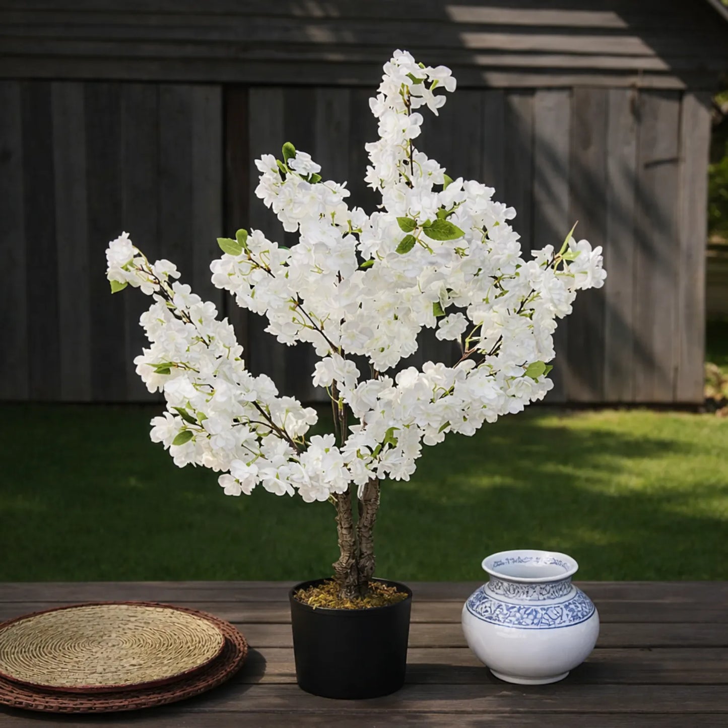 Artificial white flowering tree in a pot on a wooden table with a blurred background