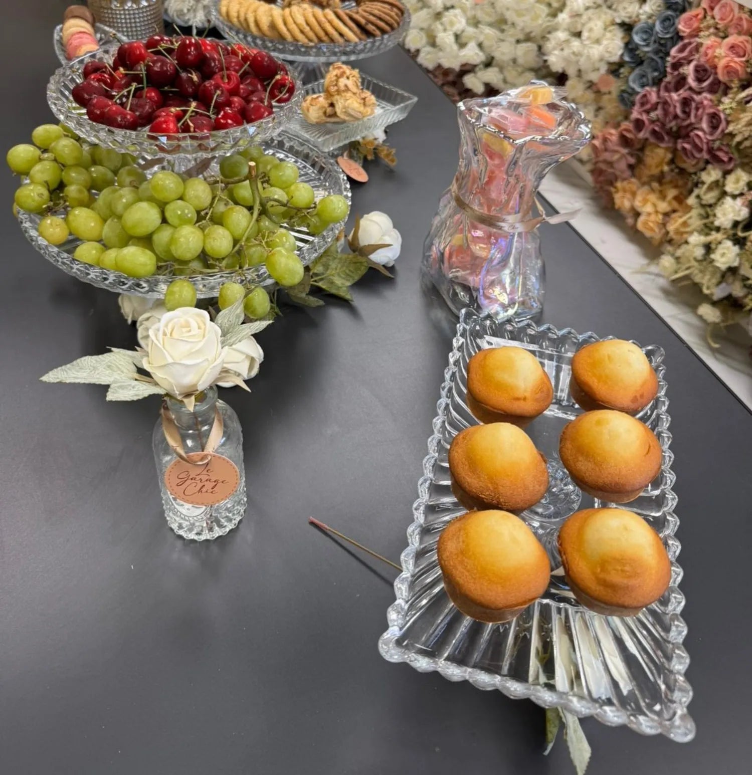 Decorative table setting with fruits, flowers, and a vase on a dark surface.
