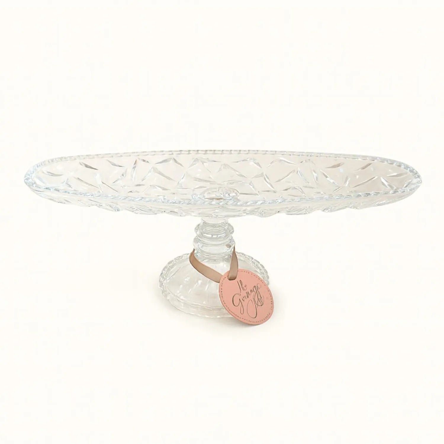 Clear glass cake stand with a pink tag on a white background