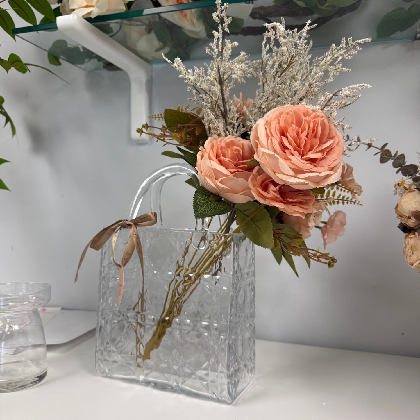 Clear glass bag with peach-colored flowers and greenery on a white surface.